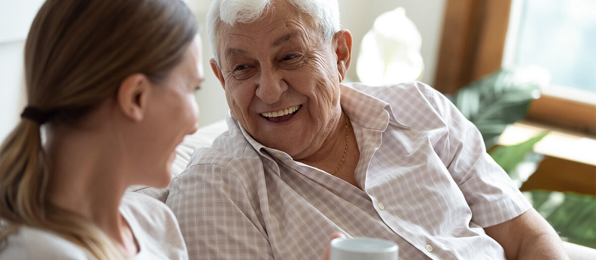 Older man laughing with a caregiver over a cup of coffee