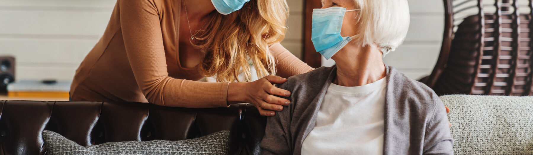 Senior woman in medical mask with social worker visiting her at home